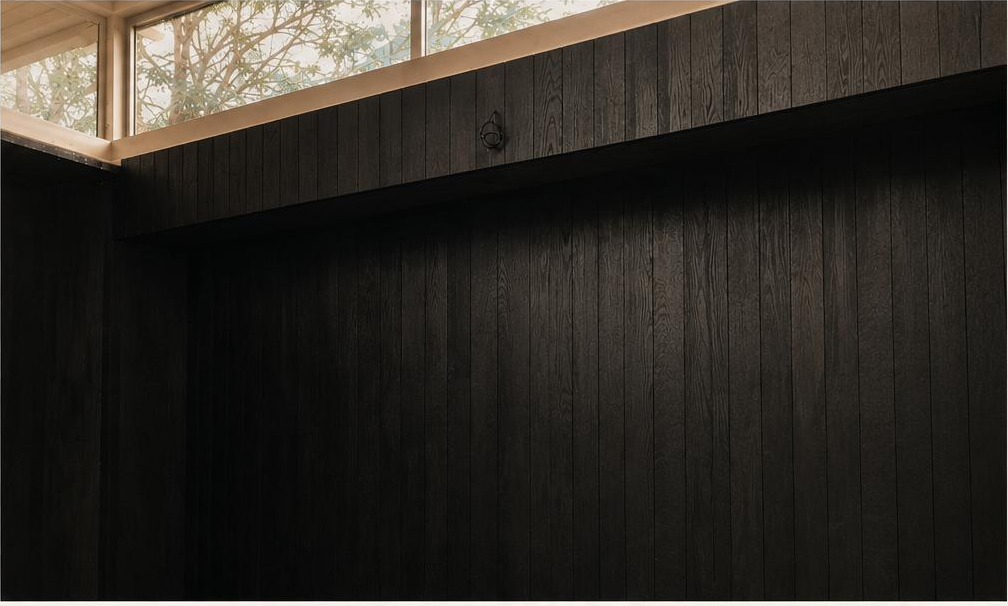 Interior view of a retail space clad in charred cedar planks, with clerestory light spilling over the wood